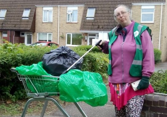 A lady holding a litter picker next to a shopping trolley with bin bags in it