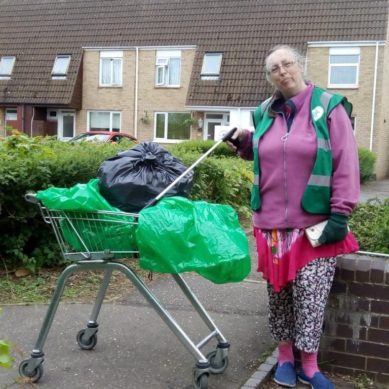 A lady holding a litter picker next to a shopping trolley with bin bags in it