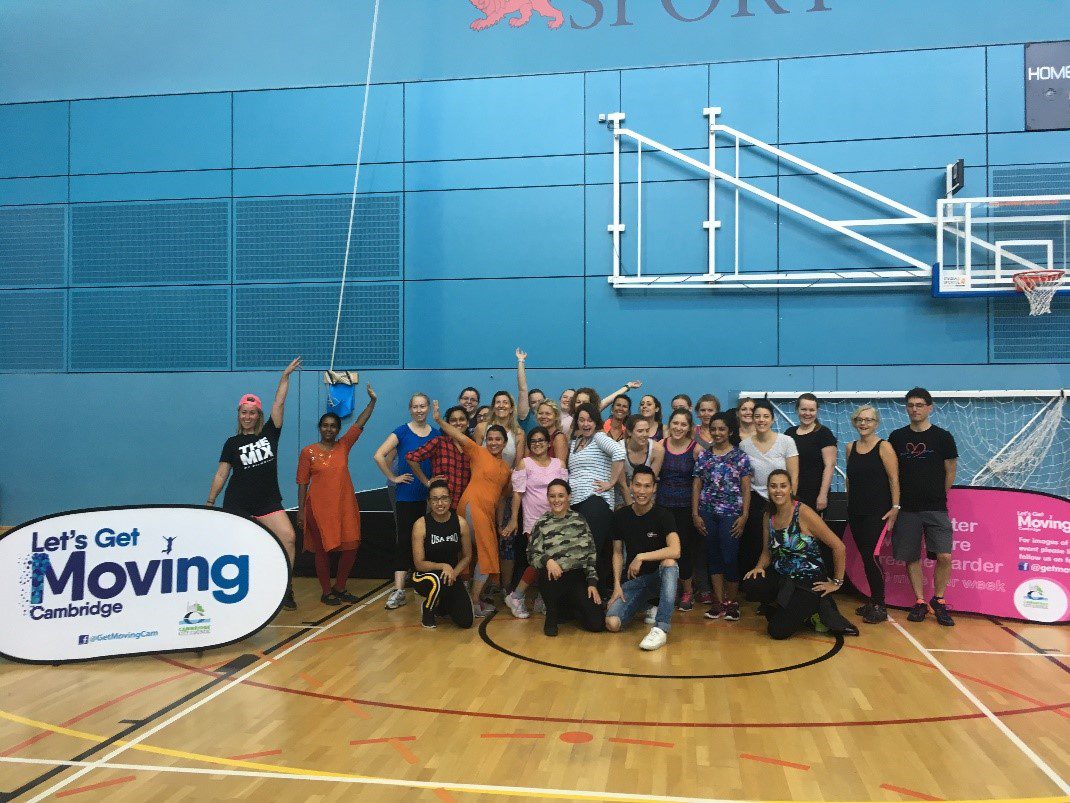 A group of men and women in a sports hall with a Let's Get Moving Cambridge sign