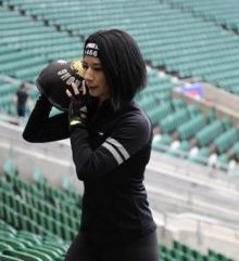 A dark haired lady wearing all black holding a weight on her shoulder in a sports stadium