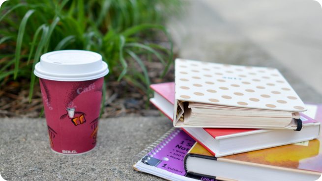 Stack of 4 books next to a coffee cup on the pavement