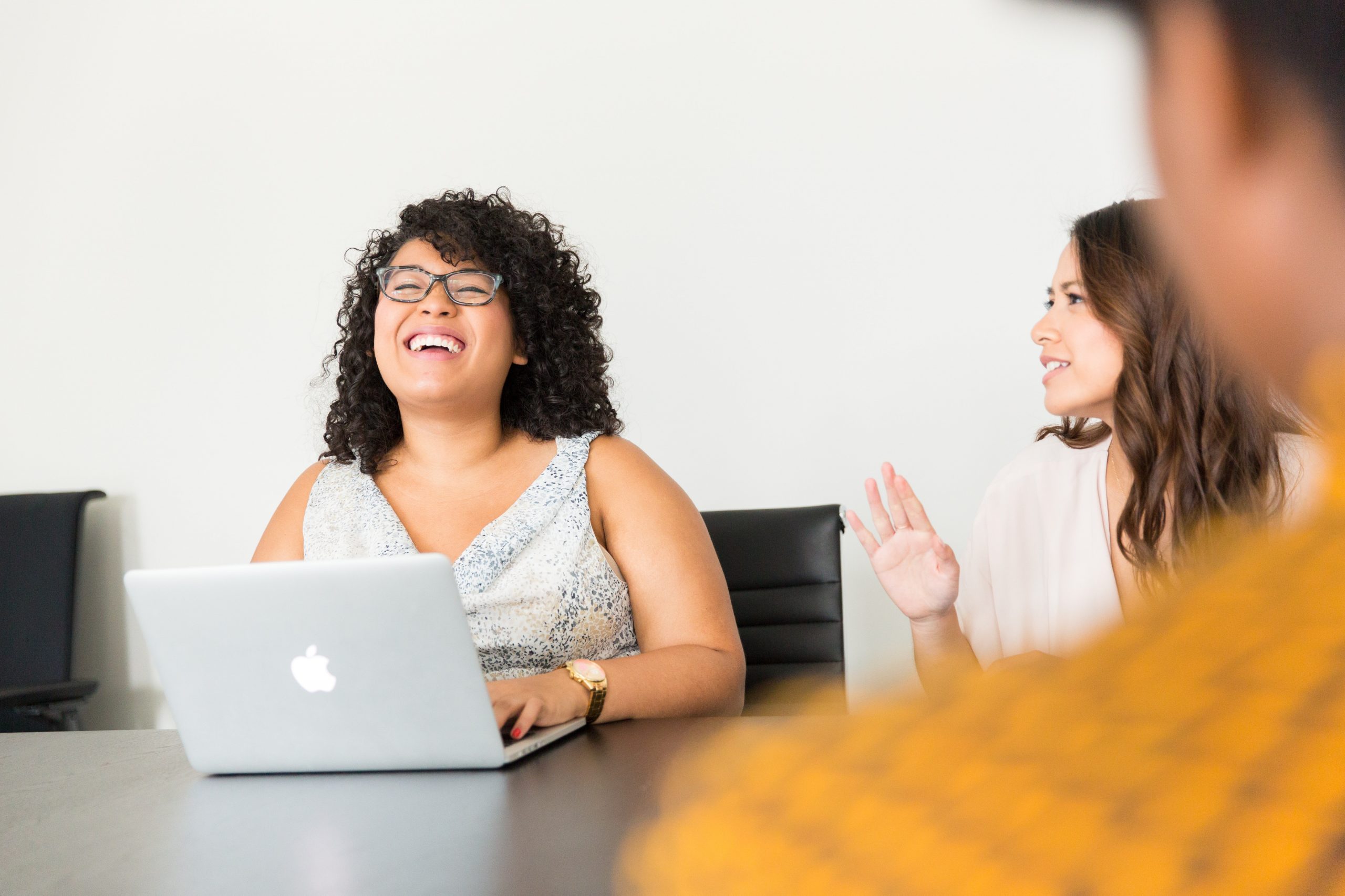 Black woman using a laptop laughing with a woman sat next to her