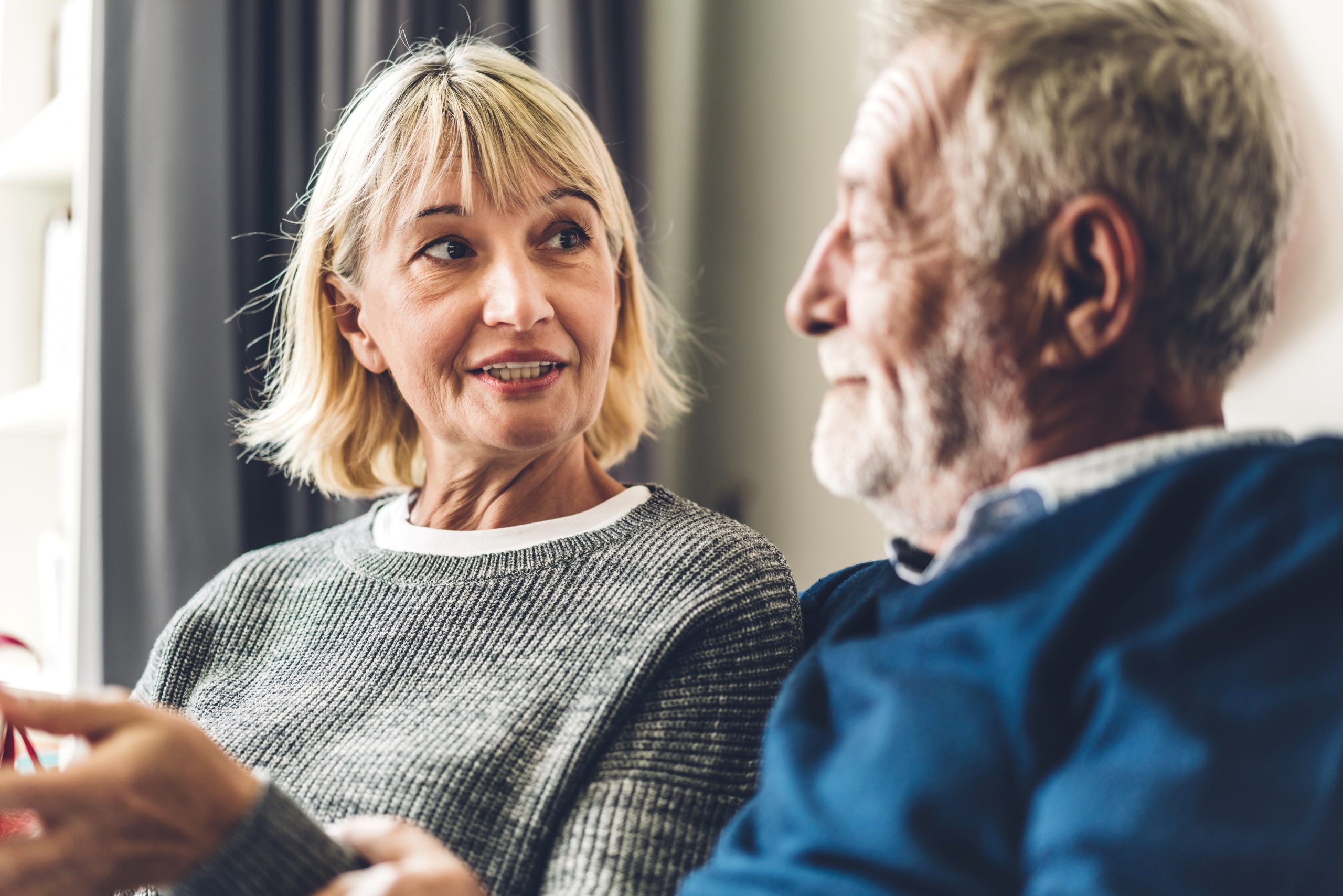 Senior couple relaxing and talking together sitting on sofa in living room at home.