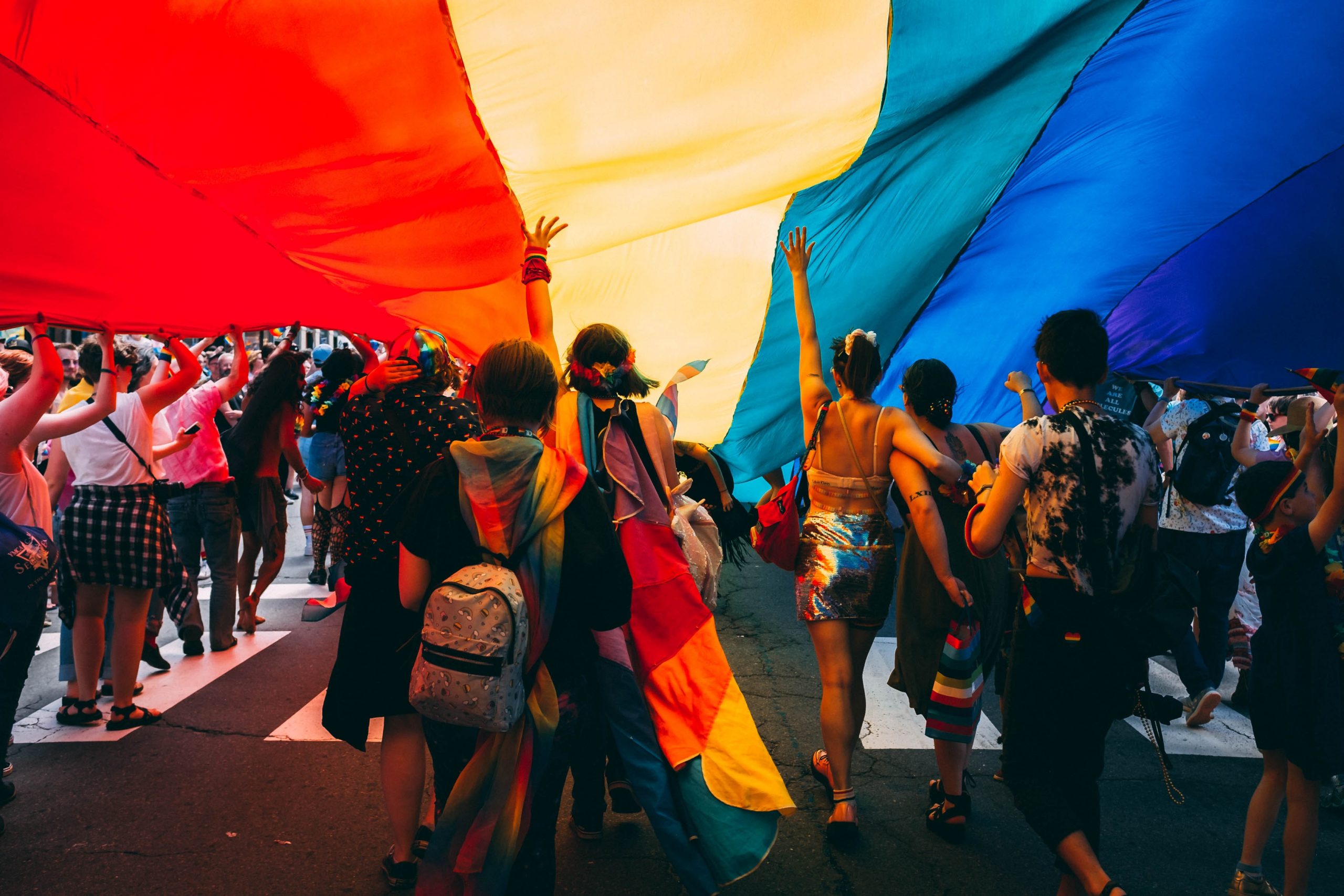 group of people under a red, yellow and blue covering walking down the street