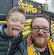 A little boy with his tongue out next to a man smiling at Cambridge United