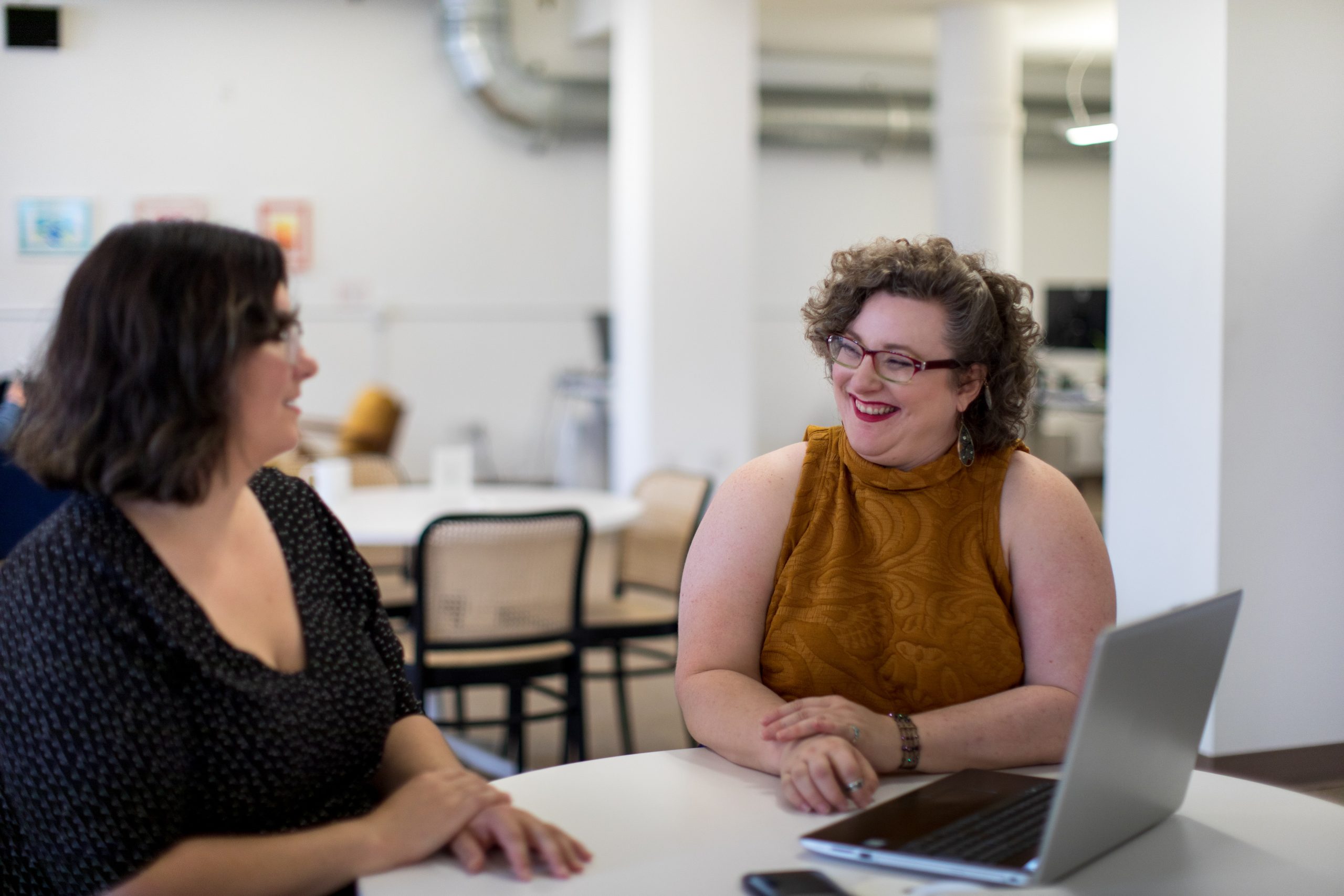 Two women sitting at a table smiling - Mental Health First Aid Training Course Cambridge