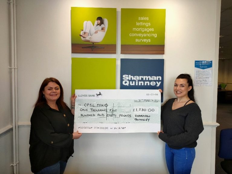 Two women in front of a Sharman Quinney sign holding a cheque for CPSL Mind for £1,580