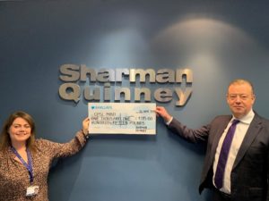 A woman and man in front of a Sharman Quinney sign holding a cheque for CPSL Mind