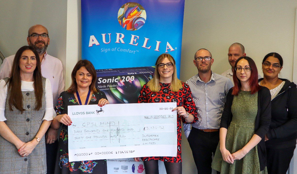 A group of men and women holding a cheque for CPSL Mind in front of an Aurelia sign