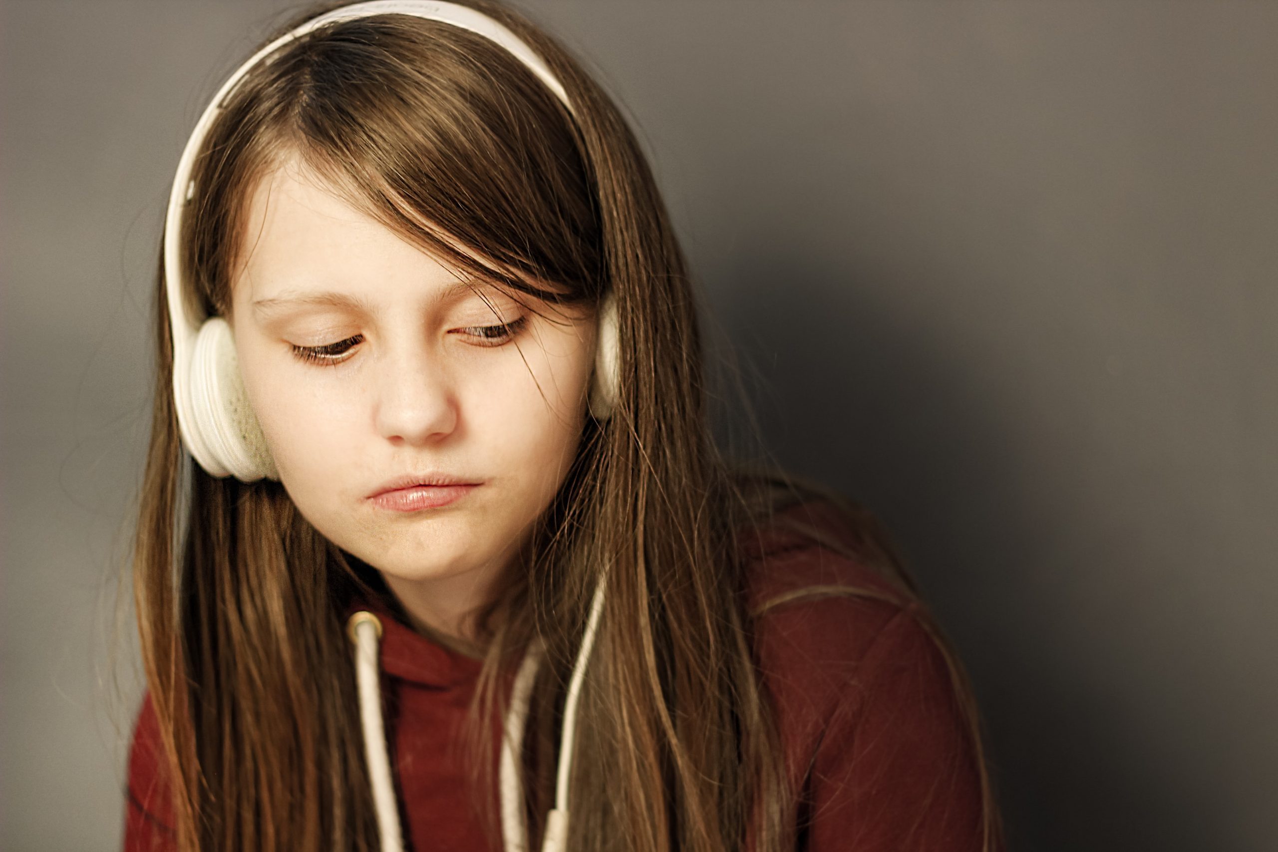 Young girl with dark hair and white headphones on looking sad