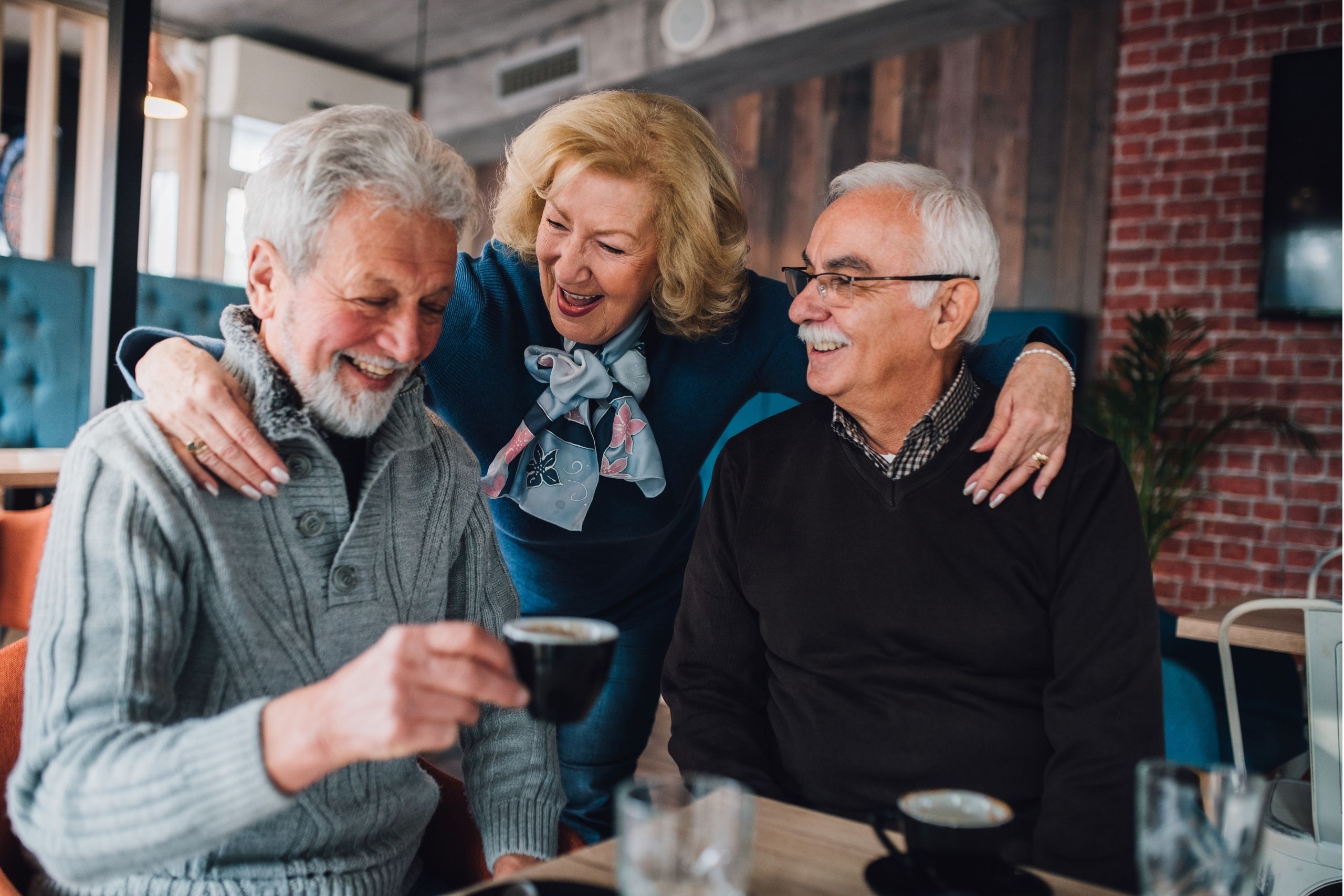 Senior female with her arms around two senior men sitting in a cafe