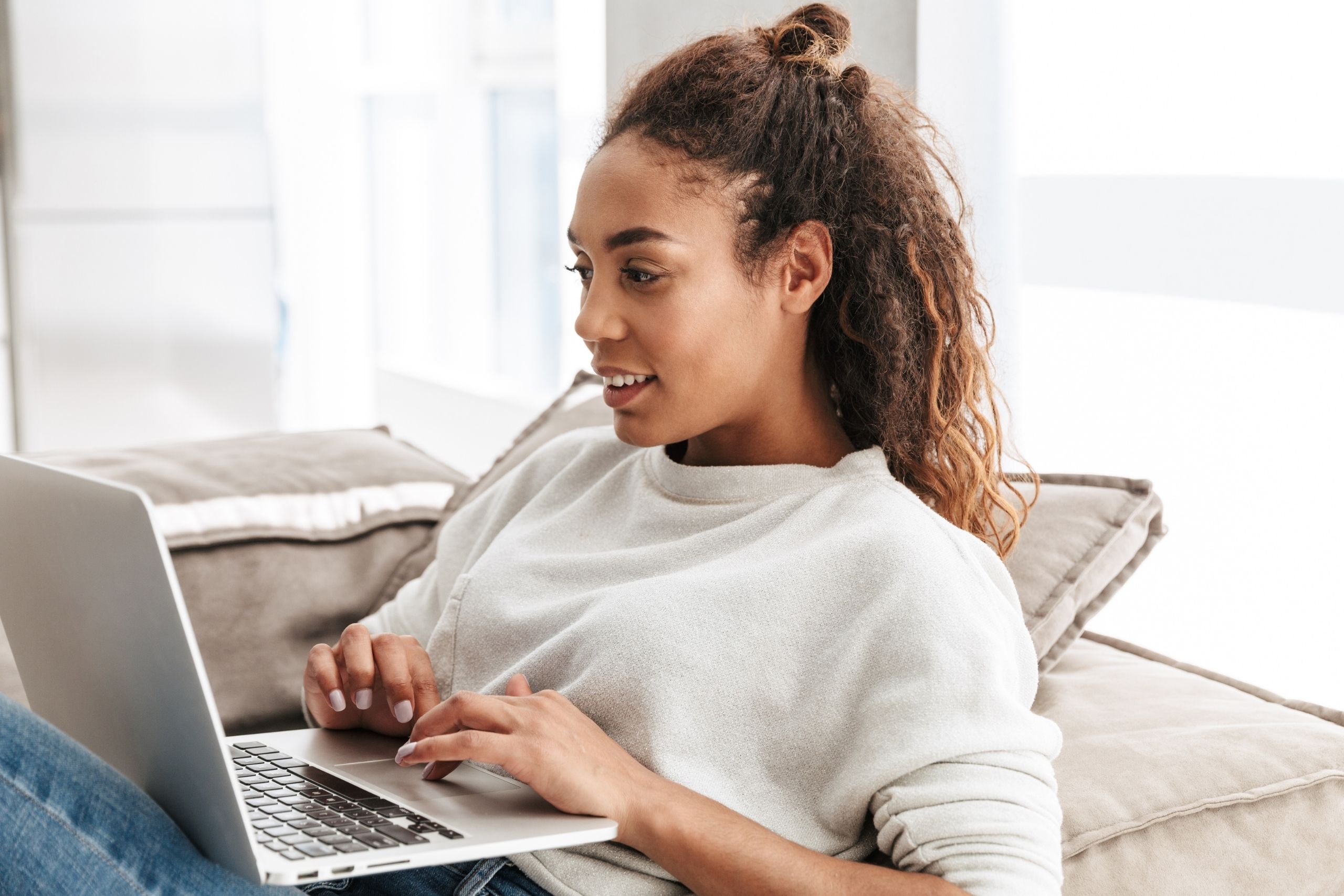Woman with half hair tied back sitting on sofa using laptop