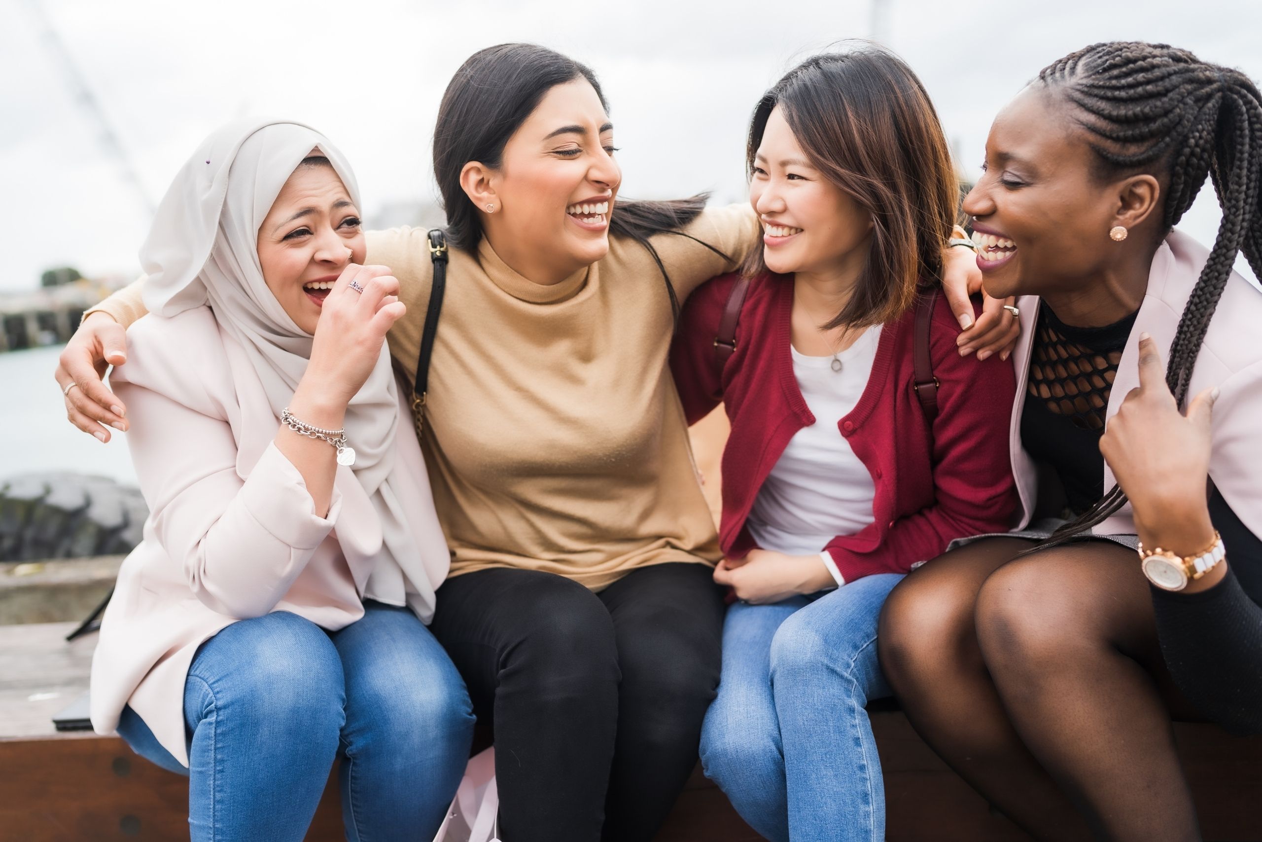 Four girls laughing together sat outside - Good Life Service