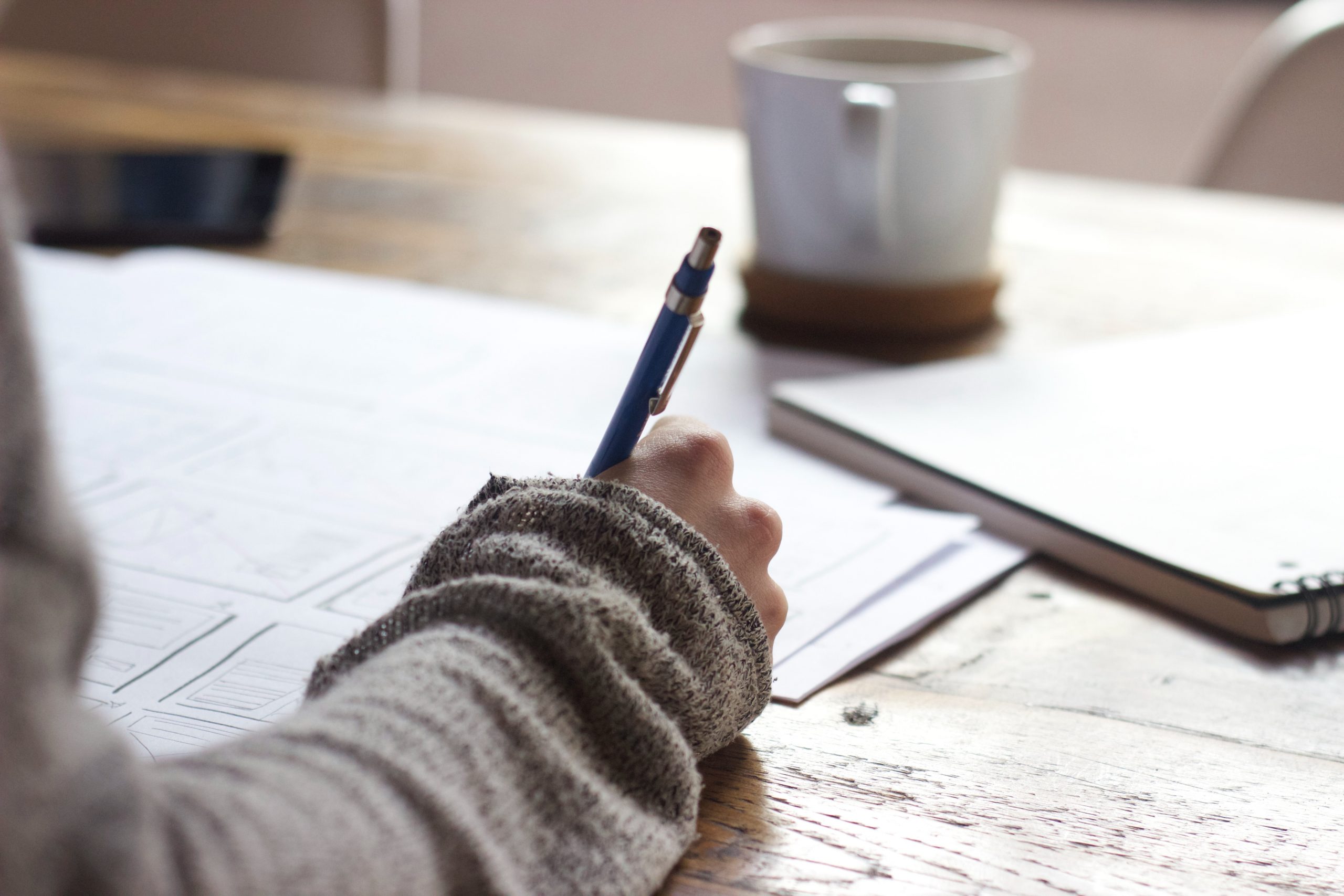 Woman in cardigan writing notes with coffee cup and tablet in background