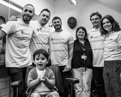 A black and white picture of a group of people wearing CPSL Mind t shirts and a little boy sat in a barbers chair