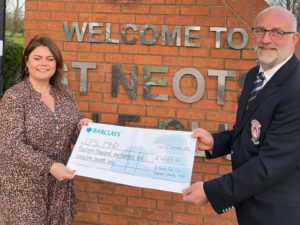 A man and women holding a cheque for CPSL Mind in front of a Welcome to St Neots Golf Club sign on a brick wall