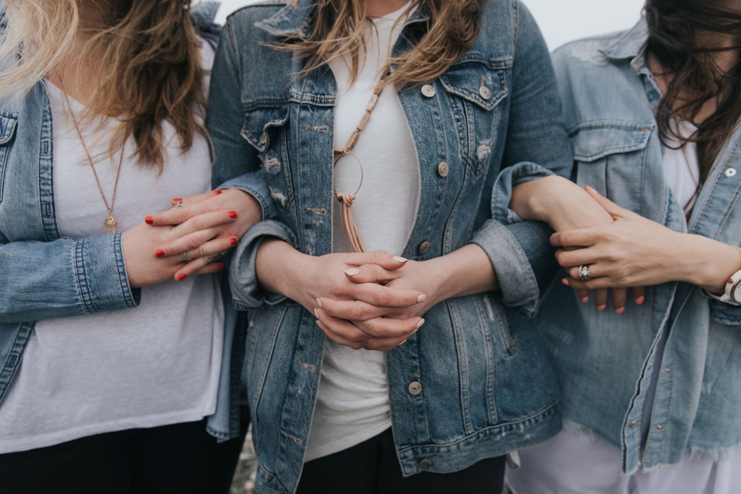 Three women in white tops and denim jackets linked arms