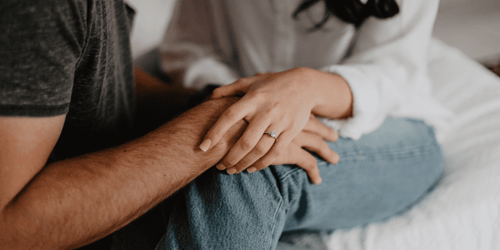 Woman holding mans hands while sitting on bed