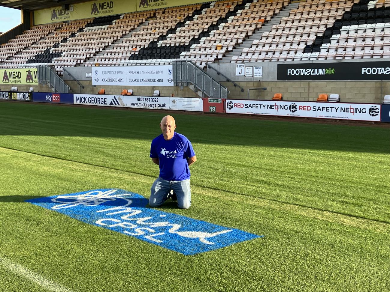 A picture of a man kneeling on a field with the CPSL Mind logo on it - Ian's walk for mental health