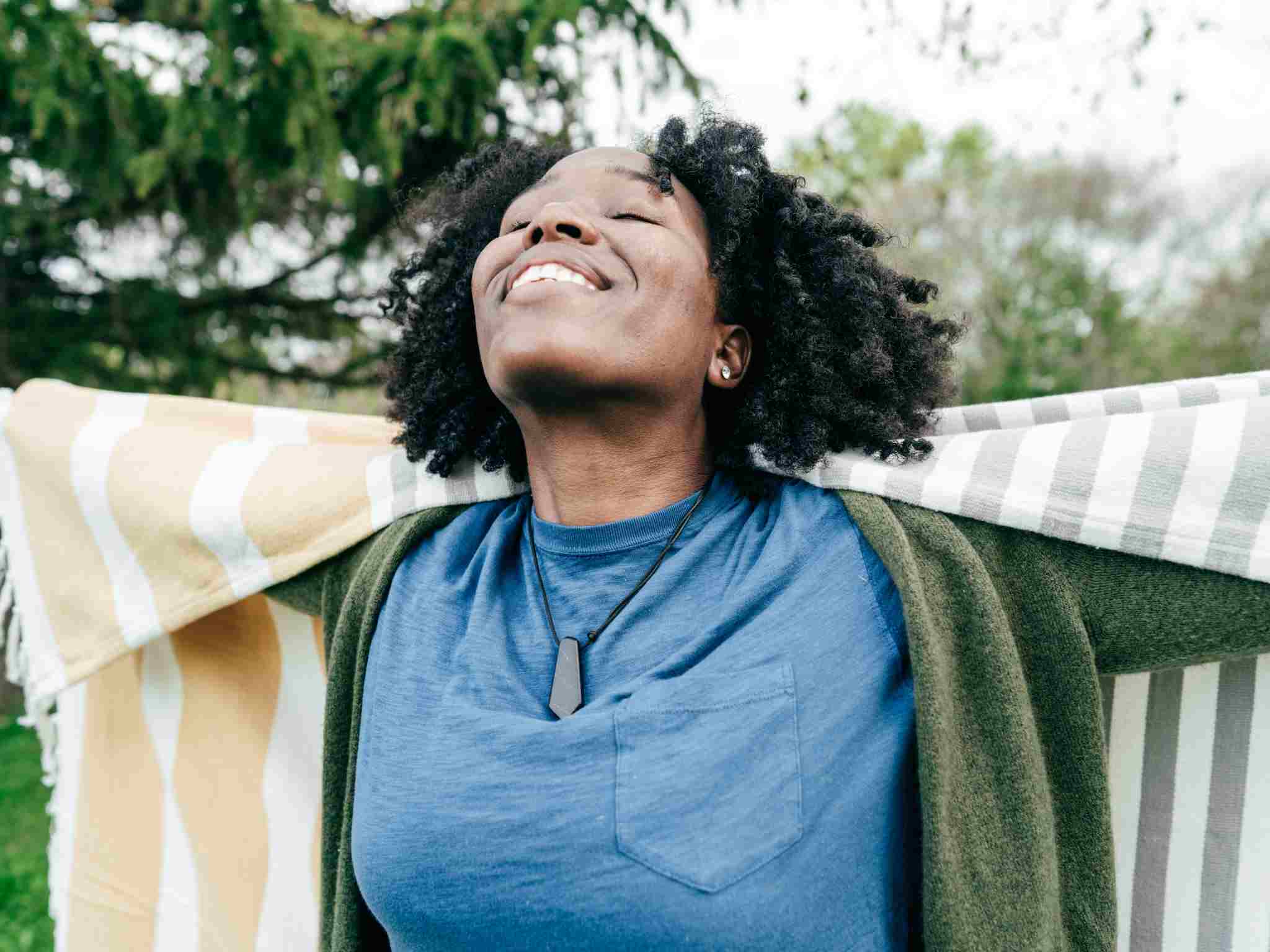 A woman smiling and looking at the sky with her eyes closed - staying well for mental health
