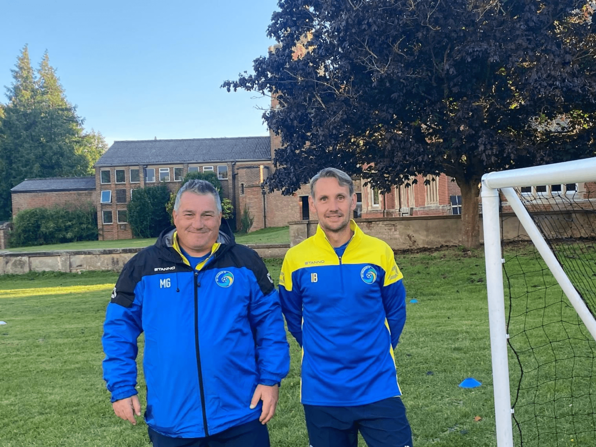Image of two men on a football pitch wearing blue sports jackets