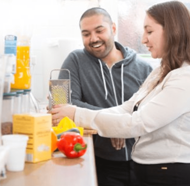 man smiling and woman with brown hair cooking in kitchen