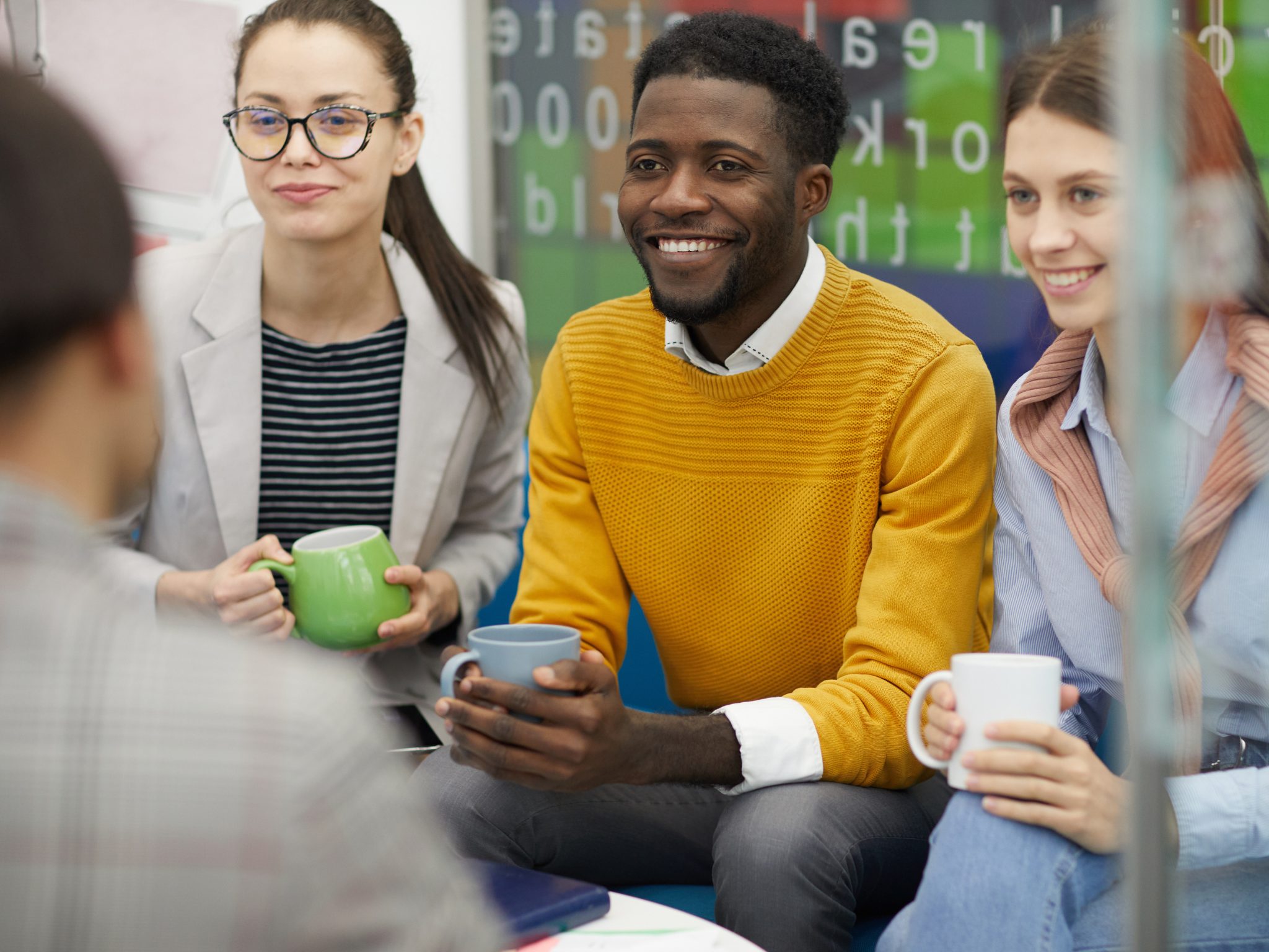 young black man and two white women holding mugs and smiling sitting in a group