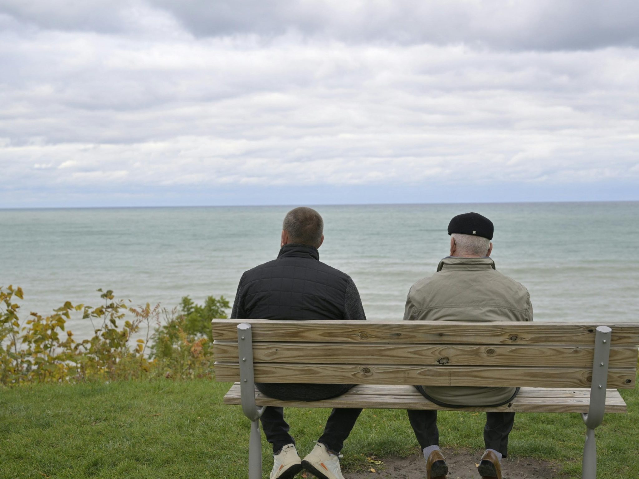 two men sitting on a bench looking out at sea