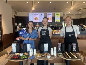 two women, one wearing blue dress and another wearing black apron and man in coffee shop 