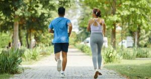 Two people jog along a park pathway surrounded by greenery.